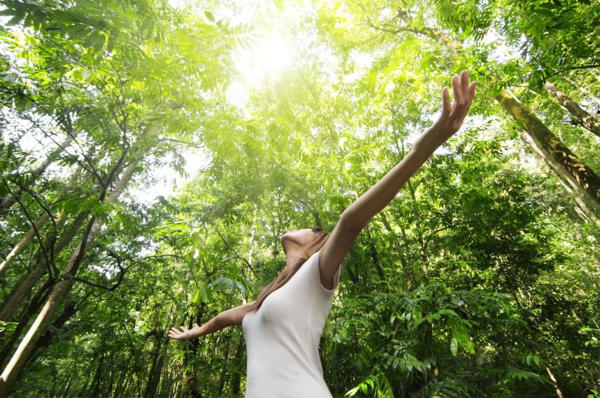 Young woman arms raised enjoying the fresh air in green forest